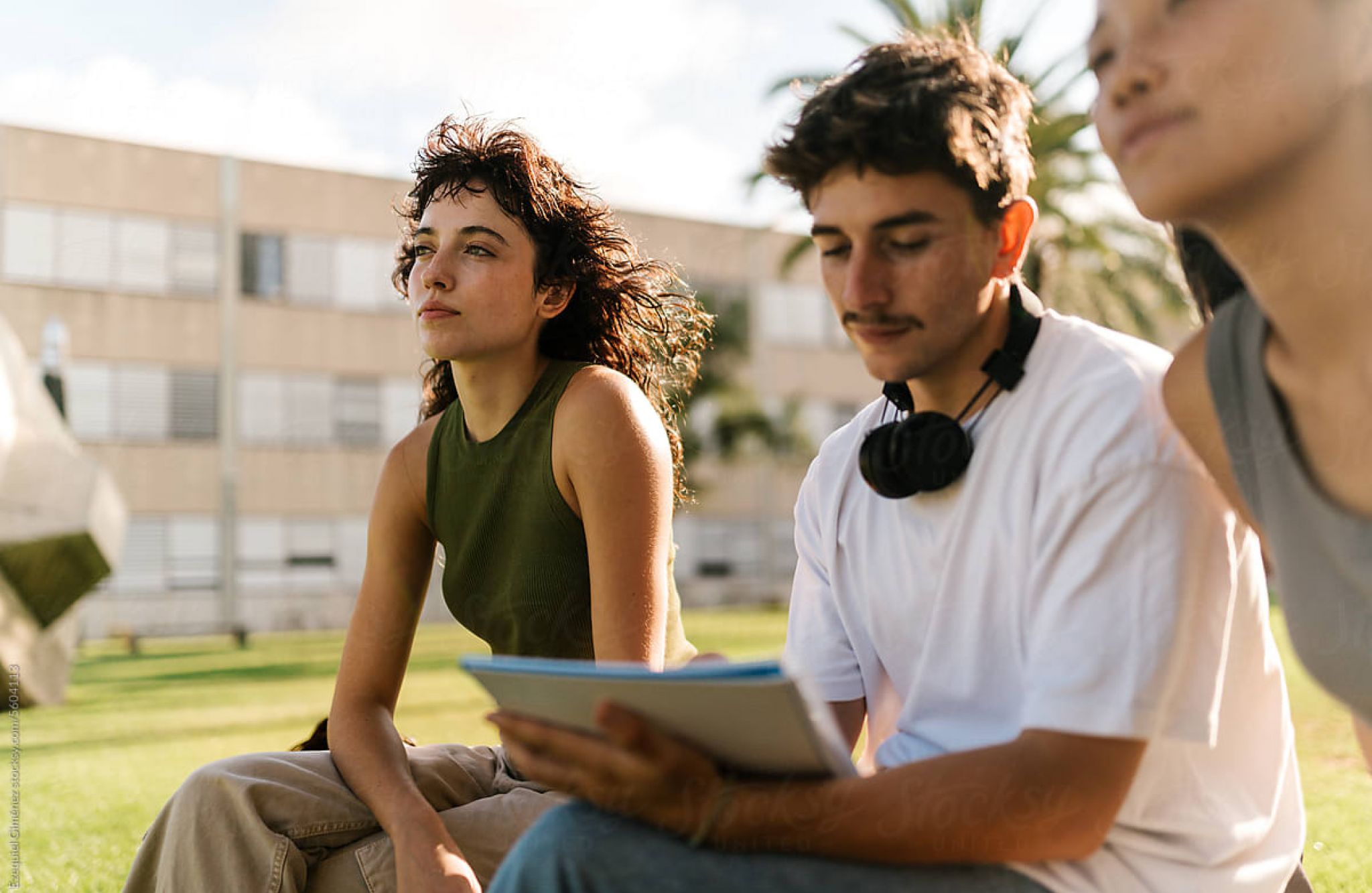 EVER College Station Three young adults sitting outside, one holding a tablet, with a building and palm trees in the background.