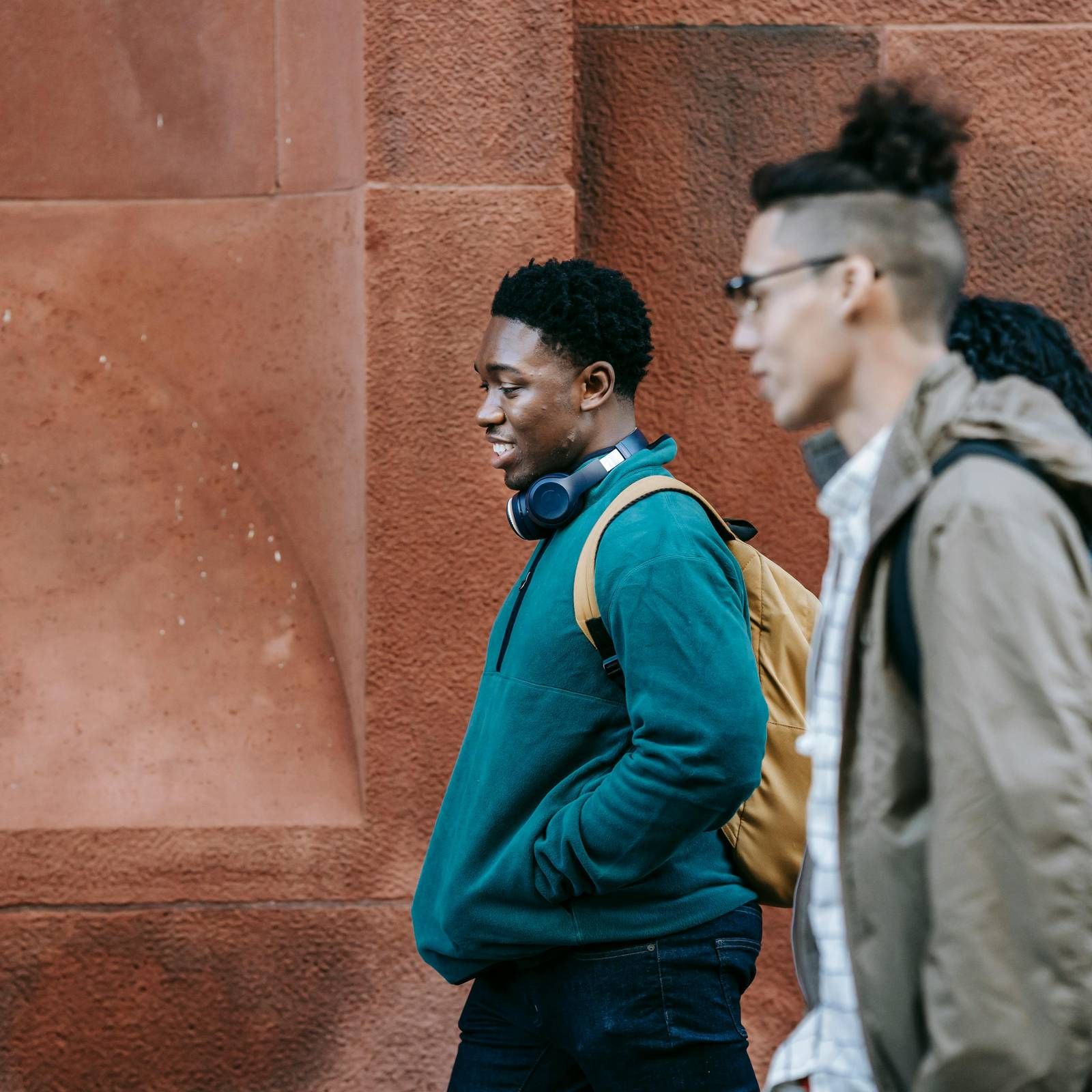 Ever College Station student living apartments Three young people walk past a red wall; one wears headphones and a backpack, another wears glasses.