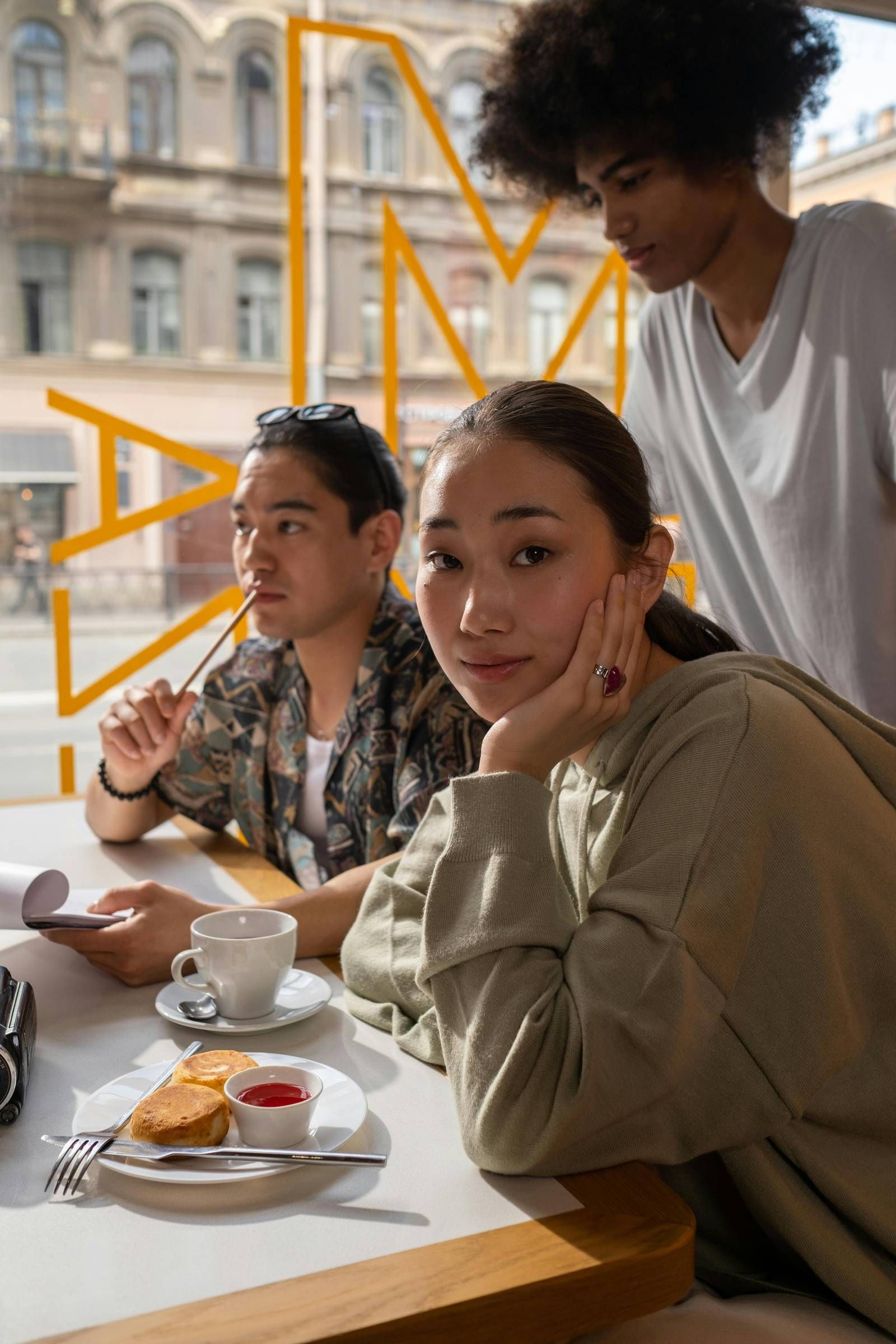 EVER College Station Three young people sit at a café table with coffee and toast, looking thoughtful near a large window.