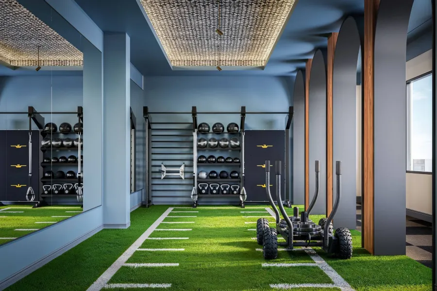 Ever College Station student living apartments Modern gym with artificial turf, kettlebells, medicine balls, sleds, and large mirrors under bright lighting.