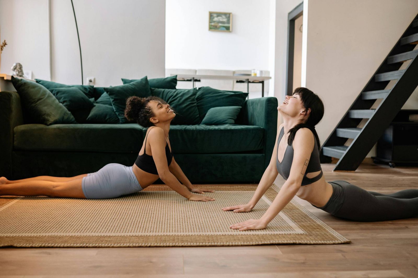 EVER College Station Two women practicing yoga indoors, both in cobra pose on a rug in a modern living room.