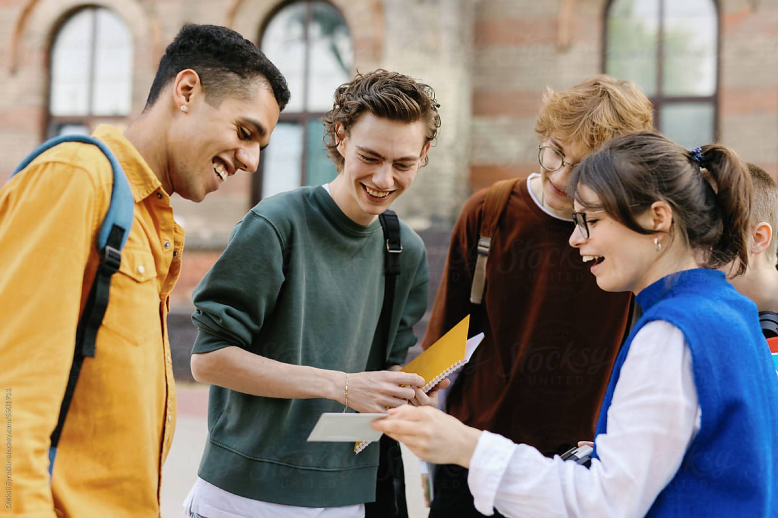 EVER College Station Four young adults smiling and looking at papers together outside a building.