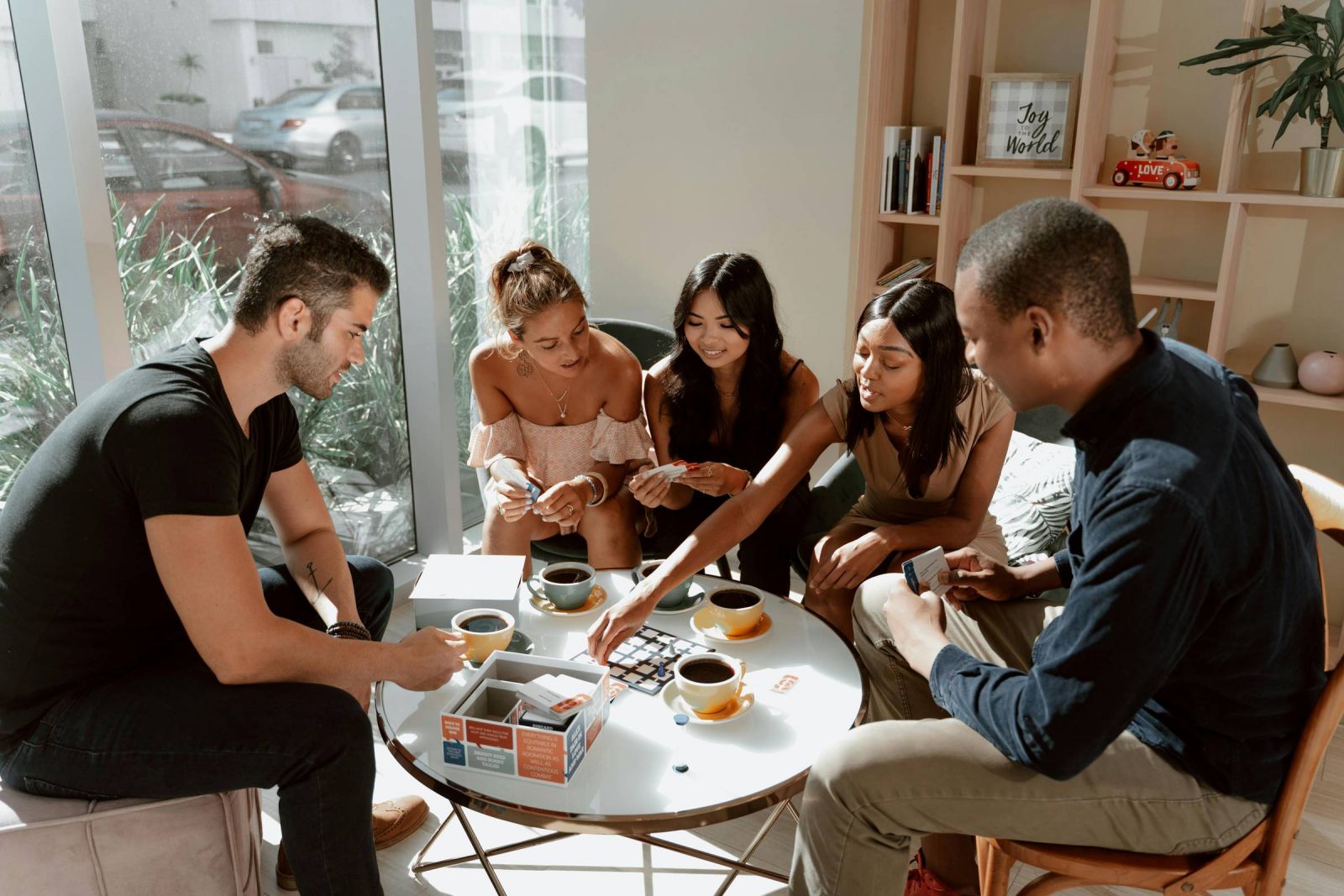 EVER College Station Five people sit around a coffee table playing a card game, smiling and chatting in a bright room.