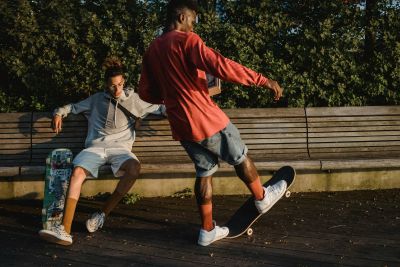 Ever College Station student living apartments Two young men hang out with skateboards, one sitting on a bench and the other skating nearby outdoors.